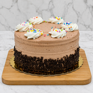 The Half and Half Layer Cake is a round chocolate vanilla cake with chocolate frosting, topped with six white whipped cream swirls and colorful sprinkles. Chocolate sprinkles coat the bottom edge, making a delightful buttercream treat.