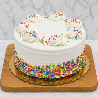 The Gold Layer Cake is a round white frosted cake topped with buttercream swirls and colorful confetti sprinkles, featuring rainbow sprinkles on the lower half and displayed on a wooden board with a gold base.