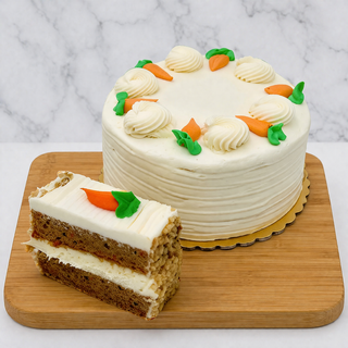 The Carrot Cake with Cream Cheese sits on a wooden board, topped with icing carrots. A slice is cut in front, displaying its moist interior and rich cream cheese frosting layers.