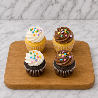 Mini Cupcakes: Four bite-sized treats—two topped with vanilla frosting, two with chocolate frosting, all sprinkled with colorful rounds—served on a wooden board against marble. Enjoy a delicious mix of Mini Cupcake flavors!.