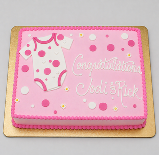 The Onesie Dots cake is rectangular and pink, topped with white and pink polka dots, a fondant baby onesie, and “Congratulations Jodi & Rick” in white icing. Displayed on a gold board—perfect for a baby shower!.