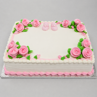 Small Booties cake: Rectangular white cake with pink frosting roses, green leaves, pink trim, and small pink baby shoes on top, set on a silver board with a blank space in the center.