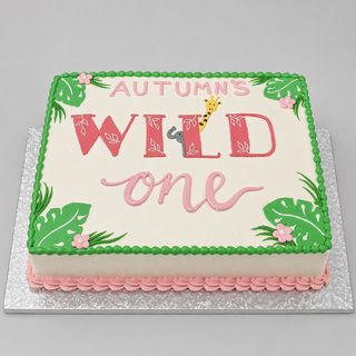 A rectangular Wild Girly cake with "Autumns Wild One" on top, a giraffe in the word "Wild," green leaves, pink flowers, and pink and green icing decorations.