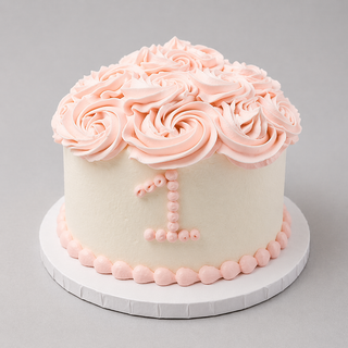 Baby Smash is a small white frosted birthday cake topped with large pink rosettes and a pink icing number 1 on the side, served on a round white board—ideal for baby’s first celebration.