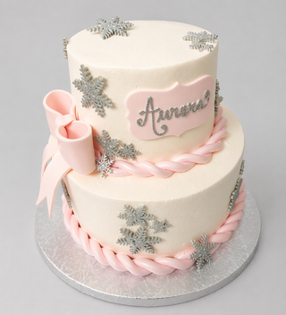 The Snowflake Bow is a two-tier white cake with pink braided fondant trim, silver snowflake bow accents, a large pink bow, and a pink plaque featuring Aurora in silver script—ideal for birthdays or baby showers.