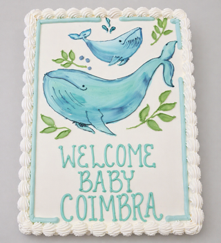 Whale Realistic cake: Rectangular custom cake with white icing, piped border, two realistic whale designs, green leaves, and "WELCOME BABY COIMBRA" in blue-green icing—ideal for animal-themed celebrations.