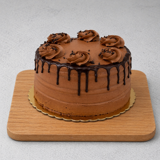 The GF Chocolate Midnight Cake is a round chocolate cake with rich ganache frosting, chocolate drip edges, and six swirls of chocolate cream on top, displayed on a wooden board.
