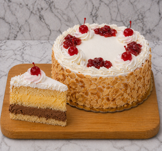 A Rum Cake sits on a wooden board, topped with whipped cream, cherries, and nuts. A slice reveals layers of homemade vanilla and chocolate custard. Marble background.