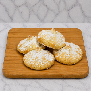 Four Raspberry Filled Shortbread Cookies, dusted with powdered sugar, rest on a small wooden board against a light marbled background.