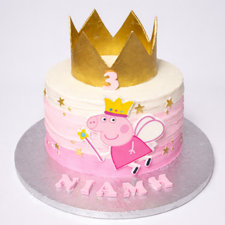 The Peppa Crown is a pink and white kids’ birthday cake with a golden Peppa crown, number 3 topper, fairy figure, gold stars, and “Niamh” in pink letters on a silver board.