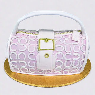 The Purse Cutout is a custom cake made to resemble a pink and white handbag, featuring a handle, gold buckle, decorative patterns, and displayed on a round gold cake board.