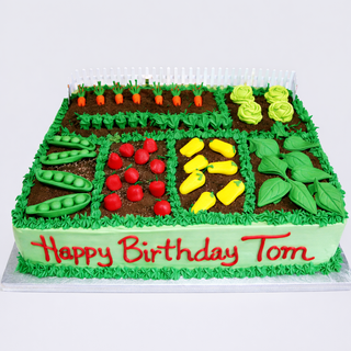 The Garden Assortment birthday cake features icing shaped like peas, carrots, lettuce, tomatoes, and corn. "Happy Birthday Tom" is written in red icing on green frosting. Custom pricing available.