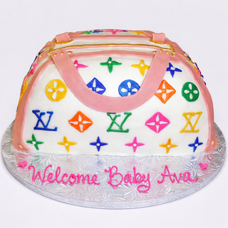 The 3D Purse cake, featuring colorful patterns and pink straps, sits on a silver board with "Welcome Baby Ava" written in pink icing.