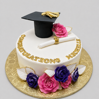 The Golden Grad cake showcases gold “Congratulations Michelle” text, a black mortarboard, diploma scroll, pink and purple sugar roses with white leaves, all presented on a gold-patterned cake board.