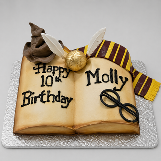 The Harry Potter Book cake is shaped like an open book and decorated with wizard hat, golden ball with wings, striped scarf, and glasses—ideal as a custom birthday cake for a magical kids celebration.