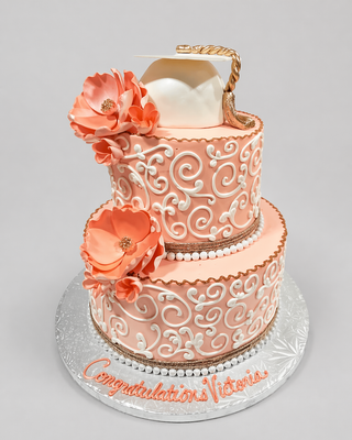Celebrate a college graduation with the Scroll Covered cake—a two-tier peach and white custom cake featuring decorative swirls, large peach flowers, a white graduation cap with gold tassel, and “Congratulations Victoria” on the base.