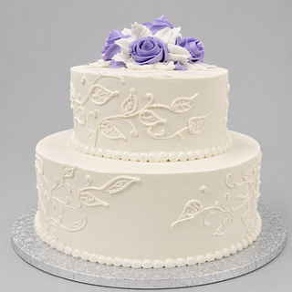 The Leaf Tier is a two-tiered white custom birthday cake adorned with piped floral decorations and purple and white fondant roses, set on a silver textured board against a plain gray background. Ideal for specialty birthday designs.