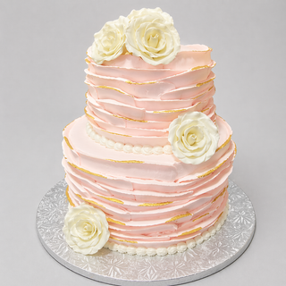 The Texture Tier is a two-tiered cake featuring pale pink textured icing, gold accents, and three large white sugar roses. Presented on a silver patterned board, this specialty birthday cake stands out against a plain gray background.