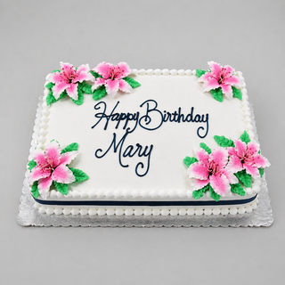 The Flower Corners cake is a rectangular white birthday cake with pink and white flower decorations, green leaves, and "Happy Birthday Mary" in blue icing—perfect for custom birthday designs and specialty cake pricing.