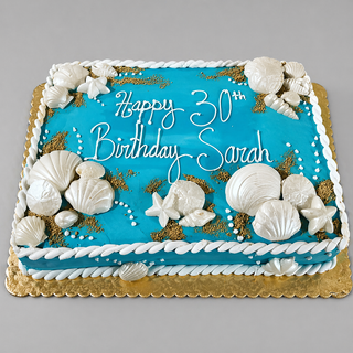 The Sand Shells cake is a rectangular blue birthday cake adorned with white seashells, starfish, gold accents, and "Happy 30th Birthday Sarah" in white icing, adding Hawaiian beach charm to your celebration.