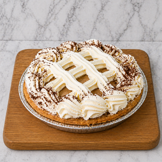 The Chocolate Mousse Pie, featuring a flaky pie crust, piped whipped cream, and chocolate shavings, rests on a wooden cutting board atop a light marble background.