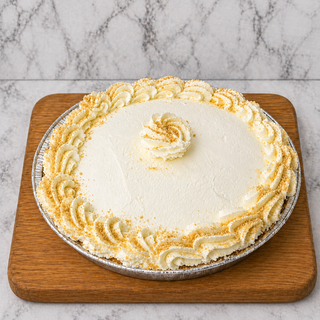 Banana Cream Pie featuring custard filling, homemade whipped cream swirls, and crumb topping is shown on a wooden cutting board with a marble background.