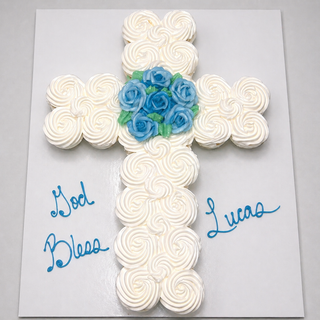 The Cupcake Cross features white swirled frosting and blue rose decorations, arranged for a religious celebration with "God Bless Lucas" written in blue icing on the board for a beautiful custom display.