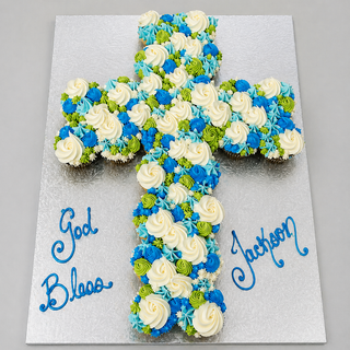 Holy Cupcakes are arranged in a cross shape on a silver board, decorated with blue, white, and green frosting flowers. "God Bless Jackson" is written in blue icing, making them ideal for religious celebrations or special occasions.