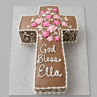 The Chocolate Cross is a cross-shaped custom chocolate cake with brown icing, pink and white flower decorations, white piping, and "God Bless Ella" written in white icing on a patterned silver board.