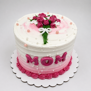The 4” Bouquet Cake is a round cake with white and pink frosting, topped with pink and white icing flowers, the word MOM in pink glitter letters on the side, and pearl-like sprinkles for decoration.