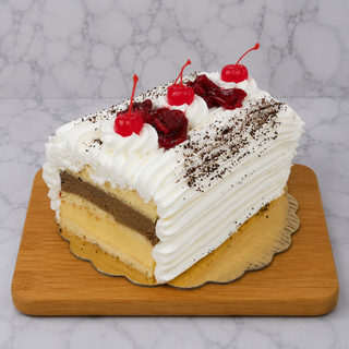 A slice of Rum Log—a layered sponge cake with chocolate and vanilla filling, topped with whipped cream, cherries, and chocolate shavings—rests on a wooden board, making for an irresistible Italian dessert.