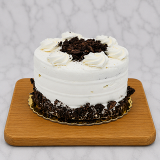The Oreo Layer Cake is a small, round cake topped and bordered with chocolate cookie crumbles over white buttercream frosting, presented on a wooden board against a marble-patterned background.