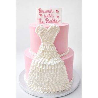 The Dress Cascade is a two-tier pink cake featuring a white icing bridal gown on the front. A plaque on top says “Brunch with The Bride” in pink lettering, accented with small heart decorations.