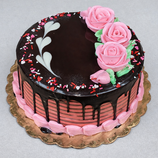 The Heart Drip is a round chocolate engagement cake with pink frosting, three pink rose decorations, green leaves, heart-shaped white icing, and red, pink, and white sprinkles. Chocolate ganache drips down the sides.