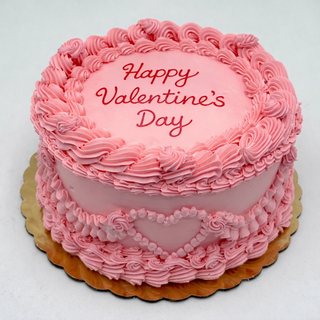 The Valentines Draped is a round pink cake with piped frosting, a heart design, and "Happy Valentines Day" written in red icing on top. It sits on a gold-colored base.